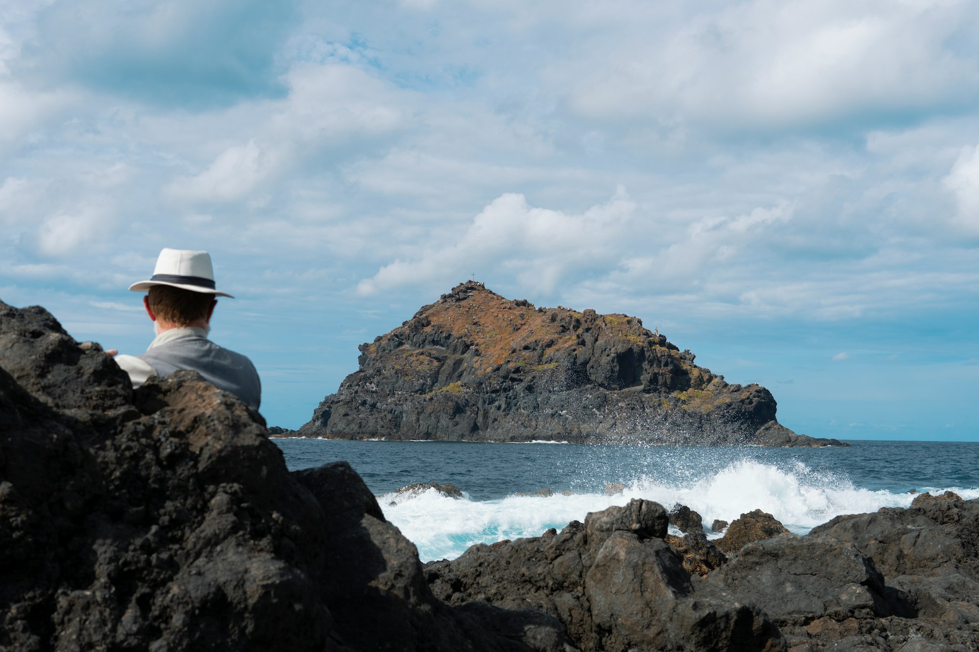 a man sitting on a rock looking out at the ocean